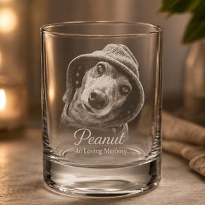 May include: A clear glass tumbler featuring a laser-etched portrait of a dog wearing a hooded sweatshirt. Below the dog, the name Peanut is engraved in a script font, followed by the text In Loving Memory in a simple sans-serif typeface.