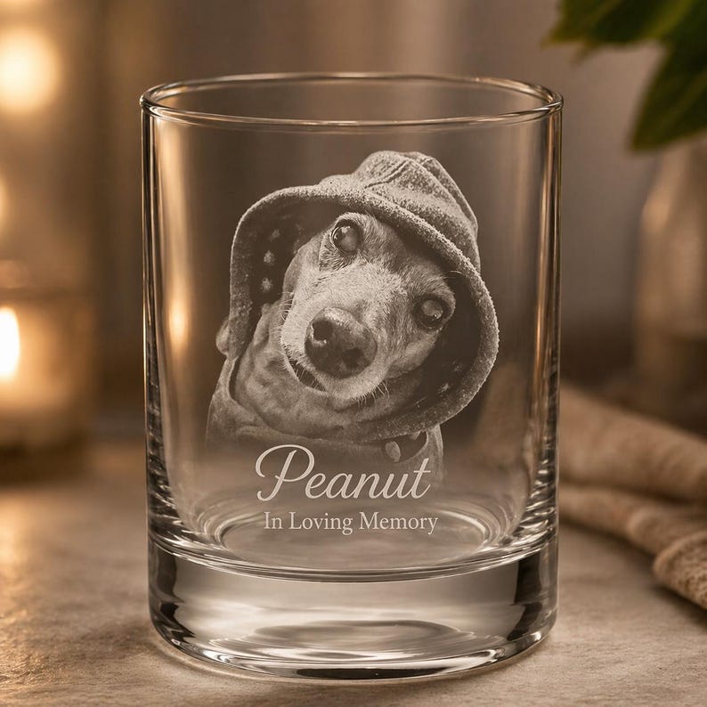 May include: A clear glass tumbler featuring a laser-etched portrait of a dog wearing a hooded sweatshirt. Below the dog, the name Peanut is engraved in a script font, followed by the text In Loving Memory in a simple sans-serif typeface.