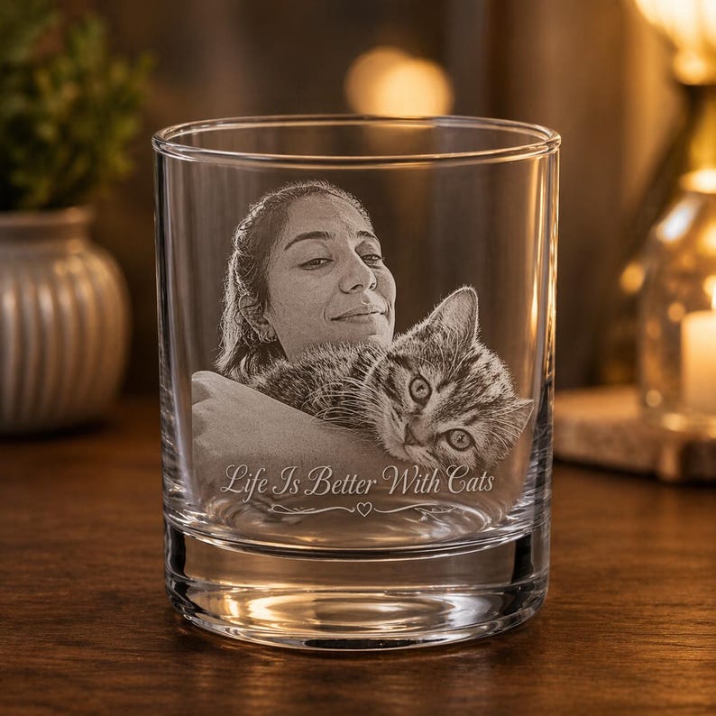 May include: A clear glass tumbler featuring a laser-etched portrait of a person holding a tabby cat. The engraving includes the text "Life Is Better With Cats" positioned below the image, accompanied by a small heart symbol centered underneath.
