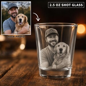 May include: A clear 2.5 oz shot glass featuring a laser-etched monochrome photographic portrait of a person wearing a baseball cap and holding a golden retriever dog. The glass has a cylindrical shape with a thick base and smooth walls.