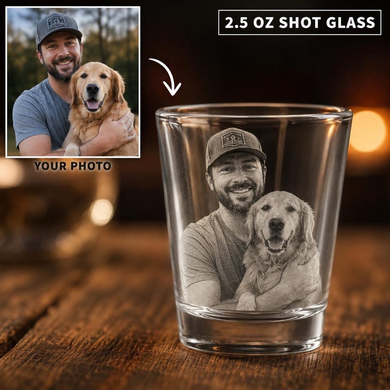 May include: A clear 2.5 oz shot glass featuring a laser-etched monochrome photographic portrait of a person wearing a baseball cap and holding a golden retriever dog. The glass has a cylindrical shape with a thick base and smooth walls.
