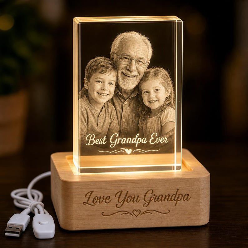May include: A rectangular glass block featuring a laser-etched image of a grandfather with a young boy and girl, with the text Best Grandpa Ever. The block sits on a light wood base engraved with Love You Grandpa and a USB power cord.