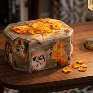 May include: An octagonal wooden box featuring a decoupage design with sepia-toned vintage photographs of people and vibrant yellow rose illustrations. The lid is adorned with scattered yellow rose petals, and additional petals lie nearby.