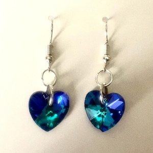 May include: A pair of heart-shaped earrings in shades of blue and teal. The earrings are suspended from silver-coloured hooks and have a faceted design. These earrings are a romantic accessory, perfect for adding a touch of colour.