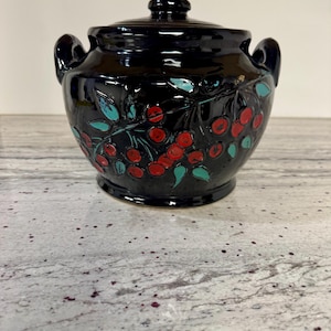 May include: A white ceramic mug with a black handle and the text "But First, Coffee" in a bold, black font. The mug is set against a blurred background, suggesting a cozy setting.