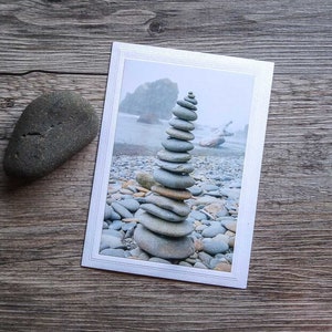 May include: A gray stone cairn stacked on a beach with a blurred background of a rocky coastline and ocean.