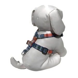 May include: A blue and orange plaid dog harness with a black buckle. The harness is on a white stuffed dog.