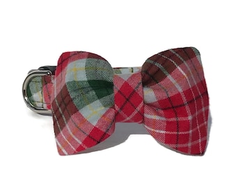 May include: A plaid bow tie for a pet, featuring a mix of red, green, and white colors. The bow tie is attached to a black collar with a silver metal clasp. The plaid pattern is a classic design.