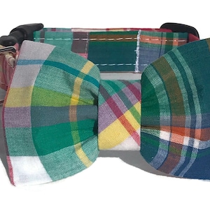 May include: A plaid dog collar with a matching plaid bow tie. The collar is red, green, blue, and white. The bow tie is tied in a knot.