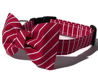 May include: A red and white striped dog collar with a matching bow tie. The collar is made of fabric and has a black plastic buckle. The bow tie is attached to the collar and is also red with white stripes.