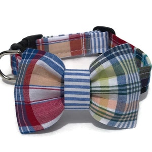 May include: A dog collar with a plaid bow tie. The collar is made of a blue and white striped fabric, and the bow tie is made of a red, blue, and white plaid fabric.
