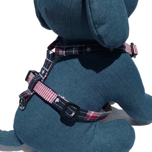 May include: A blue and white dog harness with red and white plaid accents and white stars. The harness is made of fabric and has a buckle closure.