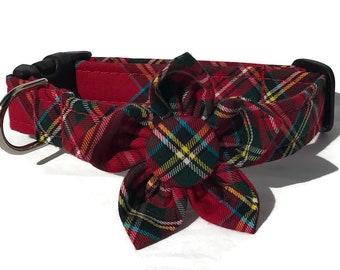 May include: Red plaid dog collar with a black buckle and a silver metal D-ring. The collar features a decorative flower made of the same plaid fabric. The plaid pattern includes red, green, yellow, and blue.