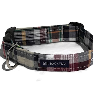 May include: A plaid dog collar with a black buckle and silver D-ring. The collar has a navy blue label that reads "B.W. BARKERY".