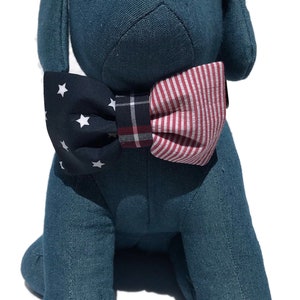 May include: A blue plush dog wearing a red, white, and blue bow tie. The bow tie has a star pattern on one side and a striped pattern on the other side.