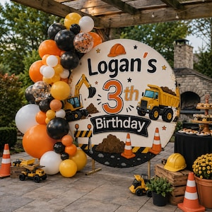 Op de afbeelding: Een rond verjaardagsbord met bouwafbeeldingen, een gele graafmachine, een kiepwagen en de tekst Logan's 3rd Birthday. Het bord is versierd met een grote ballonnenboog in oranje, zwart, wit en geel, aangevuld met oranje verkeerskegels.