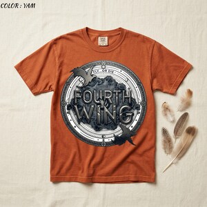 May include: A yam-colored t-shirt featuring a circular graphic with the words "FOURTH WING" in a stylized font. The graphic includes two bat-like figures and the phrase "FLY...OR DIE". Several feathers are arranged to the right of the shirt.
