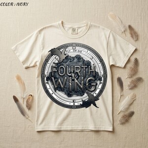 May include: Ivory-colored t-shirt featuring a circular graphic with the words "FOURTH WING" in a stylized font. The design includes bat silhouettes and the phrase "FLY...OR DIE". Feathers are arranged around the shirt.