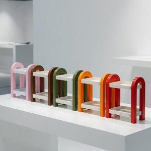 May include: A series of small, arched shelves in various colours. Each shelf has two levels and is painted in pink, brown, green, orange, and red. The shelves are displayed on a white surface.