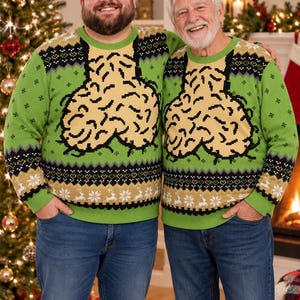 May include: A bright green long-sleeve jumper featuring a large, beige, brain-shaped graphic on the chest. The jumper includes black and white patterned bands with snowflake and reindeer motifs along the neckline, cuffs, and bottom hem.
