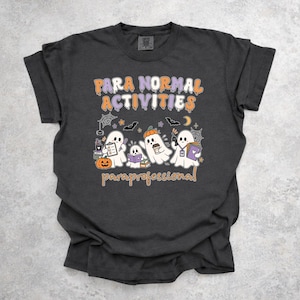 Peut inclure: Un t-shirt gris anthracite avec un motif imprimé comprenant le texte "PARA NORMAL ACTIVITIES" et "paraprofessional" en orange et blanc. Le design montre quatre fantômes blancs, des citrouilles, des livres, un presse-papier et des chauves-souris.
