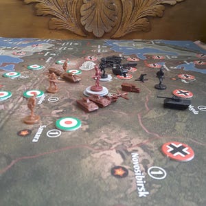 May include: A detailed board game depicting a map with miniature tanks, soldiers, and aircraft. The game board includes markers and symbols, designed for strategic military gameplay and conflict simulation.