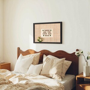 May include: A bedroom scene featuring a wooden headboard, pillows, and bedding in neutral tones. A framed artwork with the text "THESE ARE THE GOOD OLD DAYS" hangs above the bed. The room is decorated in a cozy, farmhouse style.