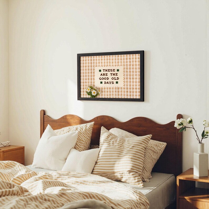 May include: A bedroom scene featuring a wooden headboard, pillows, and bedding in neutral tones. A framed artwork with the text "THESE ARE THE GOOD OLD DAYS" hangs above the bed. The room is decorated in a cozy, farmhouse style.