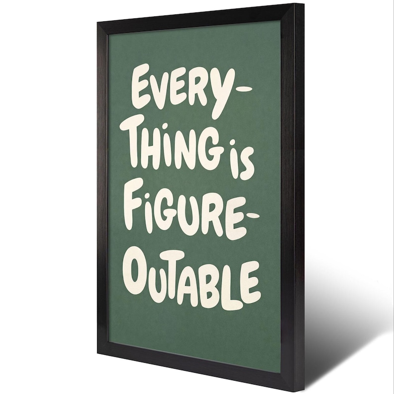 May include: A framed print with the words "EVERYTHING is FIGURE-OUTABLE" in white, bold, handwritten-style font on a dark green background. The frame is black. The print is angled slightly, casting a shadow.