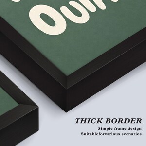May include: Close-up of framed artwork with a thick black border. The artwork has a green background with white text. The text is partially visible, with the word "Our" in large letters. The bottom right corner of the frame is visible.