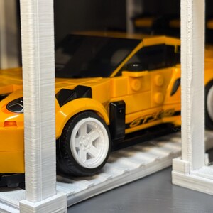 May include: A bright yellow toy sports car with white wheels and black accents. The car is a Lego model, with the words "GT3 RS" visible on the side. The car is parked in a white structure.