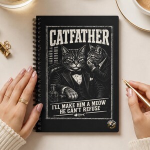 Könnte beinhalten: Ein schwarzes Notizbuch mit Spiralbindung und einer Grafik von zwei Katzen in Anzügen mit dem Text CATFATHER und I'LL MAKE HIM A MEOW HE CAN'T REFUSE. Das Cover zeigt eine Katze in einem Sessel und eine weitere, die ihr etwas zuflüstert.