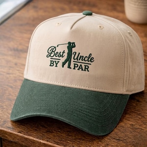May include: A beige baseball cap with a dark green brim and a dark green button on top. The front features an embroidered dark green graphic of a golfer and the text "Best Uncle BY PAR" in a combination of script and block lettering.