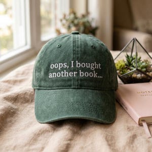 Peut inclure: Une casquette de baseball vert forêt avec une texture délavée et usée. Le panneau avant présente un texte brodé en blanc qui indique : "oops, I bought another book...". La casquette possède une calotte structurée et une visière courbée.