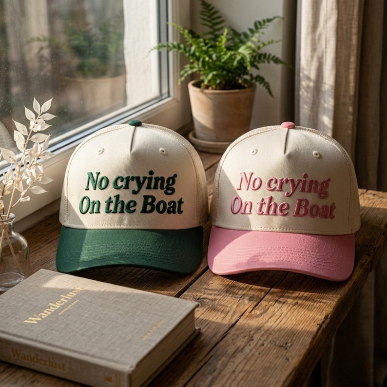 May include: Two trucker hats with off-white crowns and mesh backs. One hat features a dark green brim and dark green embroidered text that reads No crying On the Boat. The other hat has a pink brim and pink embroidered text reading No crying On the Boat.