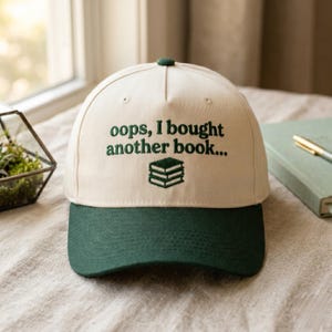 Peut inclure: Casquette de baseball crème et vert foncé avec l'inscription brodée "oops, I bought another book..." et une pile de livres. Un accessoire de mode pour les amateurs de livres, idéal pour un usage quotidien.