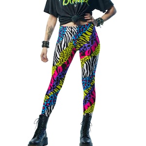 May include: Vibrant leggings featuring a patchwork design with zebra, leopard, and abstract patterns in neon pink, yellow, blue, and purple. The leggings are form-fitting and eye-catching, perfect for a bold fashion statement. The leggings are paired with black boots.