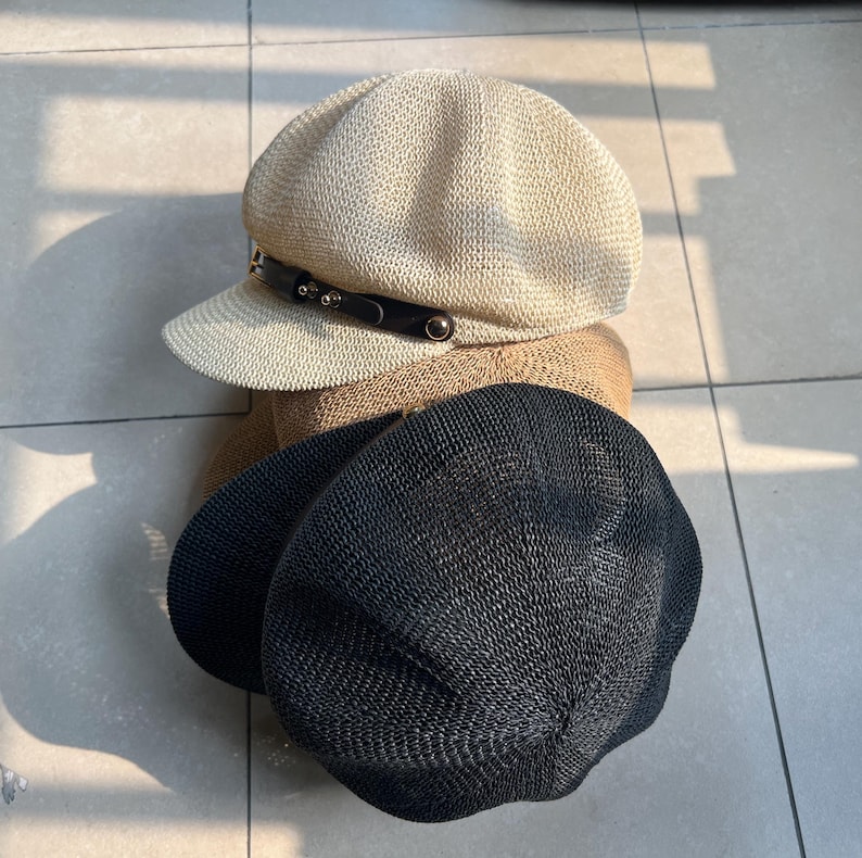 May include: Three hats in a stack. The top hat is beige with a black band and silver studs. The middle hat is tan, and the bottom hat is black. All hats have a woven texture.