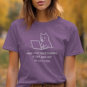 May include: A purple t-shirt with a white graphic of a dog using a laptop. The text on the shirt reads, "HAVE YOU TRIED TURNING IT OFF AND ON? I'M JUST A DOG."