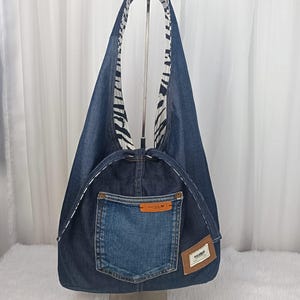 Può includere: Una borsa tote in denim con fodera a stampa zebrata a contrasto. La borsa presenta una tasca in denim blu chiaro e una toppa in pelle marrone. La borsa è progettata con una singola tracolla ed è realizzata in denim riciclato.
