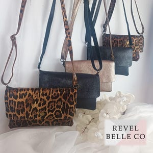 May include: A collection of crossbody bags in various colors and patterns. The bags include a leopard print, black, and metallic gold. Each bag has a long strap and a flap closure. The text "REVEL BELLE CO" is visible in the bottom right corner.