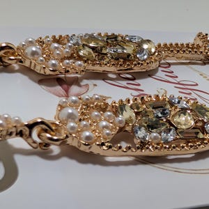 Puede incluir: Pendientes dorados con forma de copa de champ&aacute;n adornados con perlas de imitaci&oacute;n y cristales brillantes. Los pendientes presentan un dise&ntilde;o detallado con cierre de poste, perfectos para a&ntilde;adir un toque de elegancia a cualquier atuendo.