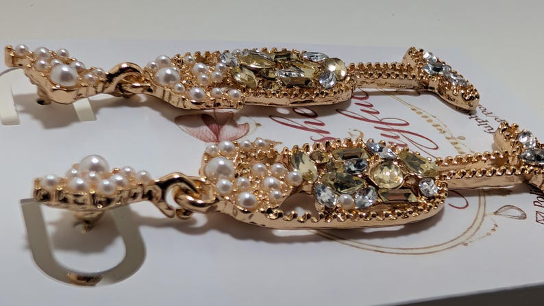 Puede incluir: Pendientes dorados con forma de copa de champ&aacute;n adornados con perlas de imitaci&oacute;n y cristales brillantes. Los pendientes presentan un dise&ntilde;o detallado con cierre de poste, perfectos para a&ntilde;adir un toque de elegancia a cualquier atuendo.