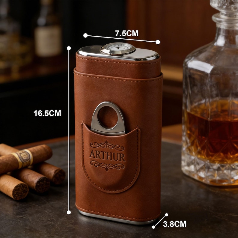 May include: A brown leather cigar case with a silver metal cigar cutter in a front pocket embossed with the name ARTHUR. The case features a top-mounted analog hygrometer and measures 16.5 cm in height, 7.5 cm in width, and 3.8 cm in depth.
