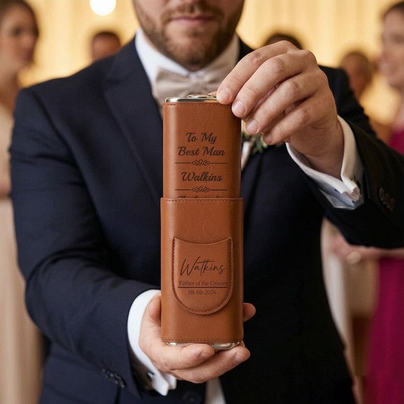 May include: A brown leather-like flask case with a flap, engraved with the text 'Watkins', 'Father of the Groom', and '08-06-2026'. A matching brown flask is partially pulled out, showing the engraved text 'To My Best Man' and 'Watkins'.