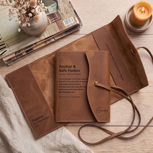 May include: A tan leather journal cover with a wrap-around tie closure. The front features the text Anchor & Safe Harbor and the name Sanden. The interior includes the phrases Together is my favourite place to be and thank you for being my greatest chapter.