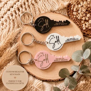 May include: Three key-shaped keyrings in black, white, and light pink acrylic. Each features a metal ring, a house icon, the word "Sold" in script, and the text "000-000-234 EMILY SMITH" along with "LONESTARREALTY.COM" printed on the surface.