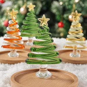 May include: Four glass Christmas tree figurines, each featuring a spiral design and a clear star topper. The trees are colored in orange, light green, dark green, and yellow, and each is mounted on a circular wooden base for display.