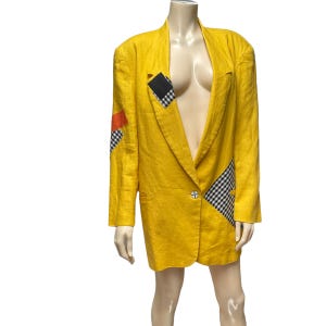 Puede incluir: Una chaqueta de lino amarilla con detalles de patchwork a cuadros en blanco y negro y negro y rojo. La chaqueta tiene un cierre de botón único y una solapa de muesca.