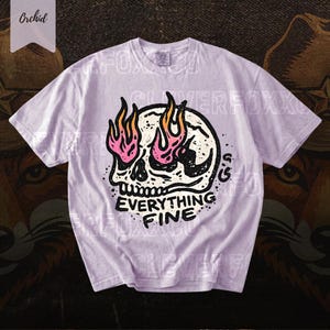 Puede incluir: Camiseta de color lila claro con un dise&ntilde;o de calavera con llamas rosas y naranjas. El texto "EVERYTHING FINE" est&aacute; debajo. La camiseta tiene mangas cortas y cuello redondo.